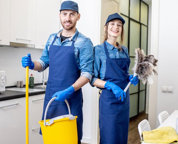 Portrait of a couple as a professional cleaners in uniform standing together with cleaning tools indoors